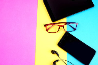 Glasses, digital tablet and smartphone with headphones on colorful background