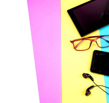 Glasses, digital tablet and smartphone with headphones on colorful background