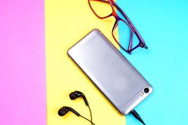 Glasses, coffee cup and smartphone with headphones on colorful background