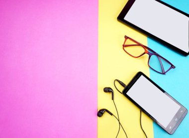 Glasses, digital tablet and smartphone with headphones on colorful background