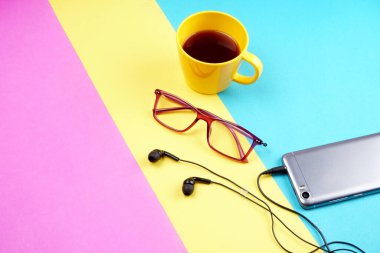 Glasses, coffee cup and smartphone with headphones on colorful background