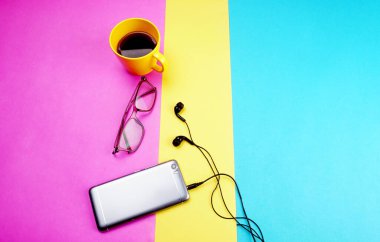 Glasses, coffee cup and smartphone with headphones on colorful background