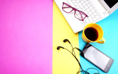 Laptop, glasses, coffee cup and smartphone with headphones on colorful background
