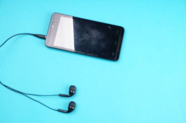 Smartphone with headphones on turquoise background