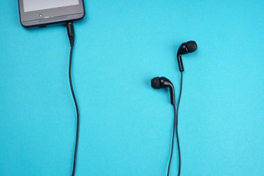 Smartphone with headphones on turquoise background