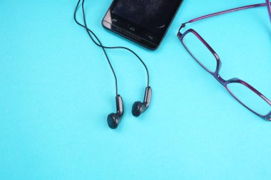 Glasses and smartphone with headphones on turquoise background