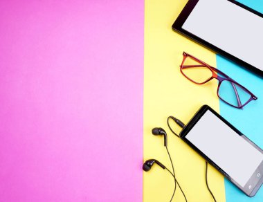 Glasses, digital tablet and smartphone with headphones on colorful background             