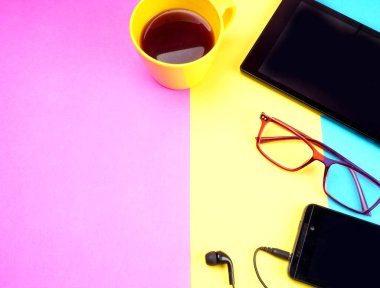 Glasses, coffee cup, digital tablet and smartphone with headphones on colorful background             