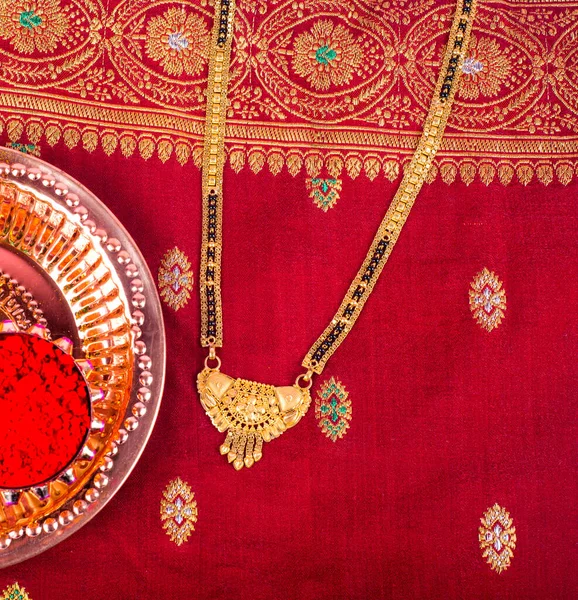 Mangalsutra or Golden Necklace to wear by a married hindu women, arranged with traditional saree with haldi, kumkum and grain rice on plate. Indian Traditional Jewellery.