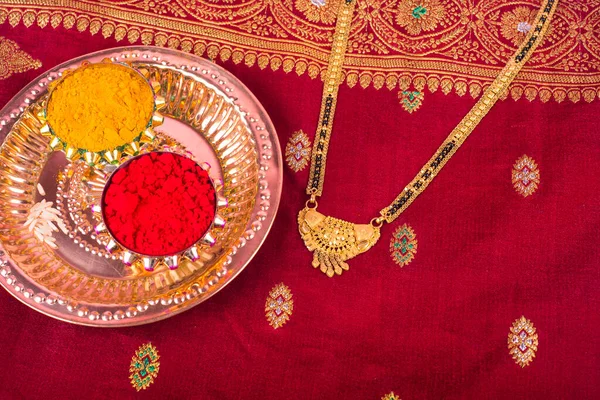 Mangalsutra or Golden Necklace to wear by a married hindu women, arranged with traditional saree with haldi, kumkum and grain rice on plate. Indian Traditional Jewellery.