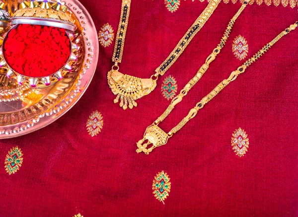 Mangalsutra or Golden Necklace to wear by a married hindu women, arranged with traditional saree with haldi, kumkum and grain rice on plate. Indian Traditional Jewellery.