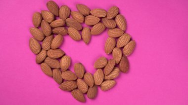 almond nuts in a heart shape on a pink background.