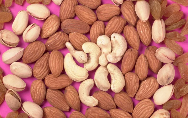Variety mix of dried fruits and nuts on a pink background. Concept of Healthy fitness super food