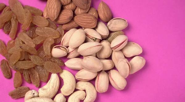 Variety mix of dried fruits and nuts on a pink background. Concept of Healthy fitness super food