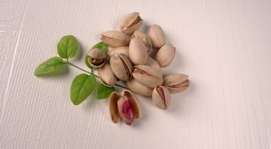 Heap of pistachios with green leaves on white background