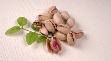 Heap of pistachios with green leaves on white background