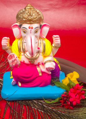 Tavus kuşu tüyü ve kırmızı arka planda çiçekler olan güzel Ganesha Hindu heykeli.