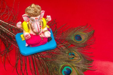 Kırmızı arka planda tavus kuşu tüyü olan güzel Ganesha Hindu heykeli