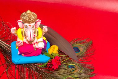 Tavus kuşu tüyü ve kırmızı arka planda çiçekler olan güzel Ganesha Hindu heykeli.