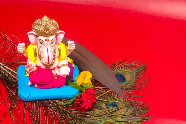 Tavus kuşu tüyü ve kırmızı arka planda çiçekler olan güzel Ganesha Hindu heykeli.