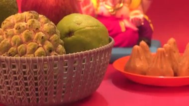 Ganesha Hindu heykeli ve kırmızı arka planda meyveli kase.