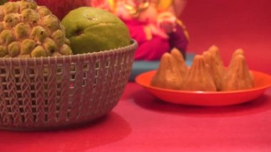 Ganesha Hindu heykeli ve kırmızı arka planda meyveli kase.