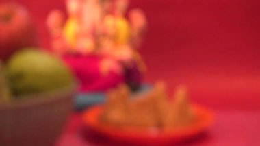 Ganesha Hindu heykeli ve kırmızı arka planda meyveli kase.