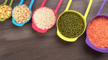 Ahşap arka plandaki renkli kaselerde pişmemiş nabız, tahıl ve tohumlar.