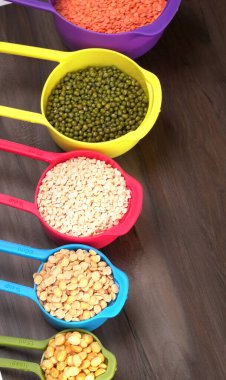 Ahşap arka plandaki renkli kaselerde pişmemiş nabız, tahıl ve tohumlar.