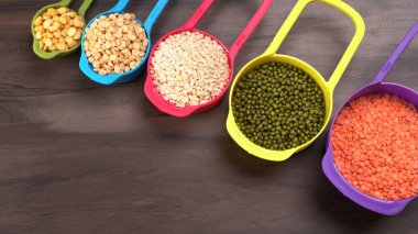 Ahşap arka plandaki renkli kaselerde pişmemiş nabız, tahıl ve tohumlar.