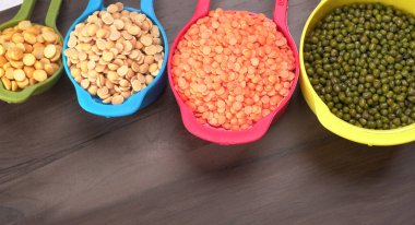 Ahşap arka plandaki renkli kaselerde pişmemiş nabız, tahıl ve tohumlar.