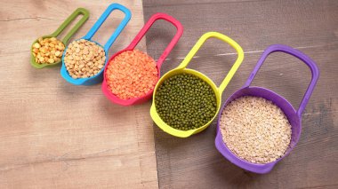 Ahşap arka plandaki renkli kaselerde pişmemiş nabız, tahıl ve tohumlar.