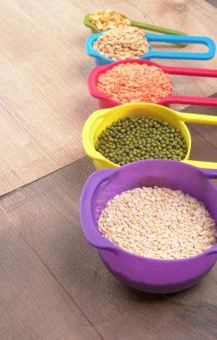 Ahşap arka plandaki renkli kaselerde pişmemiş nabız, tahıl ve tohumlar.