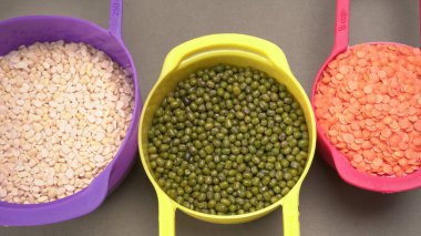 Pişmemiş nabızlar, tanecikler ve tohumlar gri arka planda renkli kaselerde