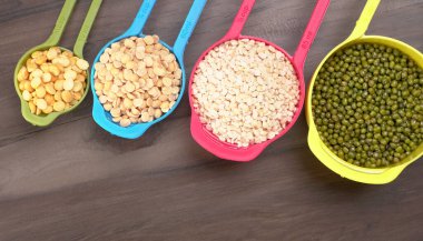 Ahşap arka plandaki renkli kaselerde pişmemiş nabız, tahıl ve tohumlar.