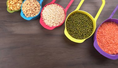 Ahşap arka plandaki renkli kaselerde pişmemiş nabız, tahıl ve tohumlar.