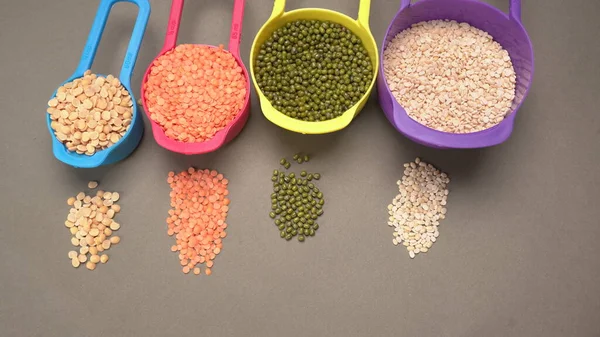 Uncooked pulses, grains and seeds in colorful bowls on grey background