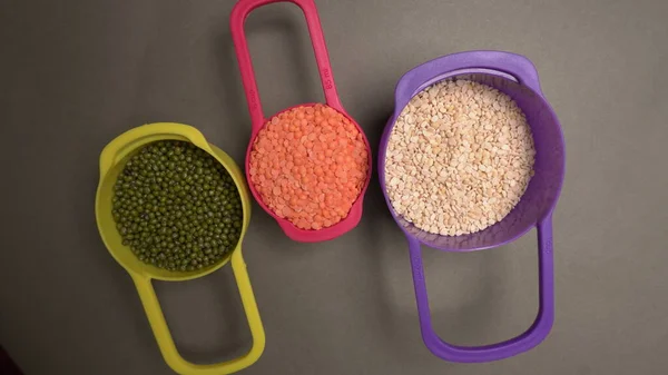 Uncooked pulses, grains and seeds in colorful bowls on grey background