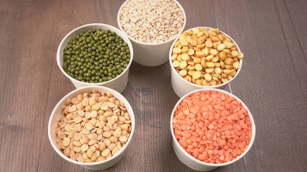 Uncooked pulses, grains and seeds in bowls on wooden background