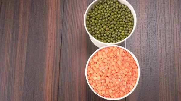 red lentils and green peas in bowls on wooden background