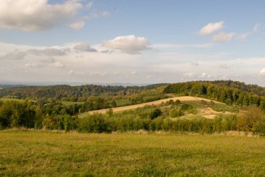 Yüksek dağlara ve açıklıklara bakan manzara. Uzakta ağaçlar ve binalar var..