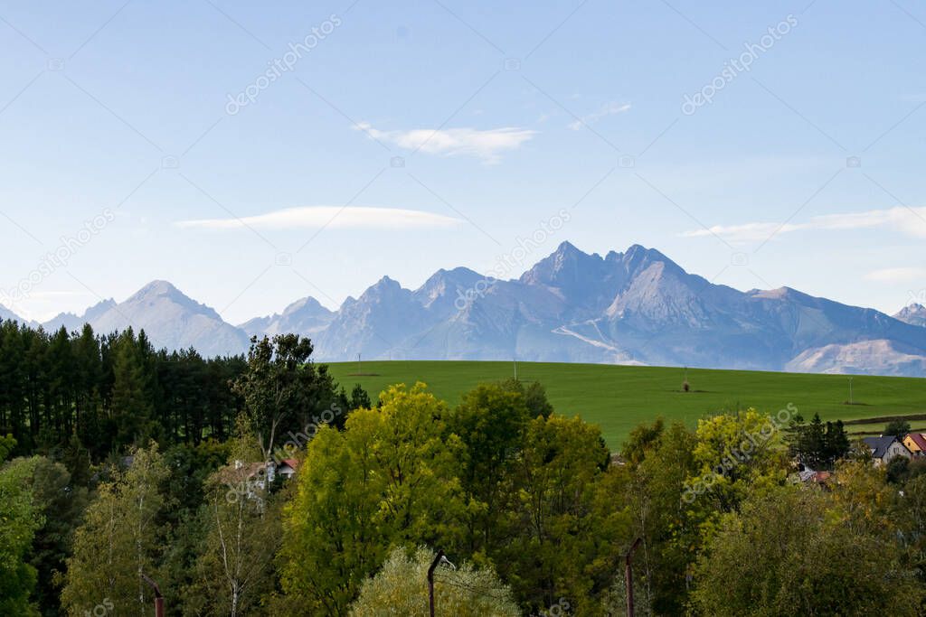 Landscape with a view of high mountains and clearings. In the distance a strip of trees and buildings.