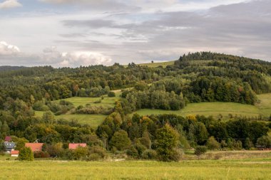 Yüksek dağlara ve açıklıklara bakan manzara. Uzakta ağaçlar ve binalar var..