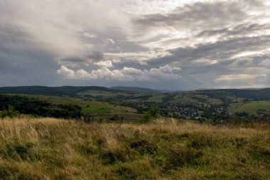 Yüksek dağlara ve açıklıklara bakan manzara. Uzakta ağaçlar ve binalar var..