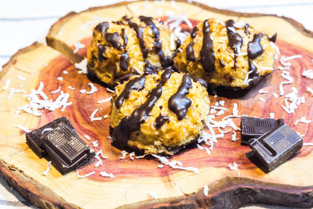 Close Up of Coconut Macaroons with Dark Chocolate Drizzle Served on Cherry Wooden Board Garnished with Chocolate Pieces and Coconut Shavings