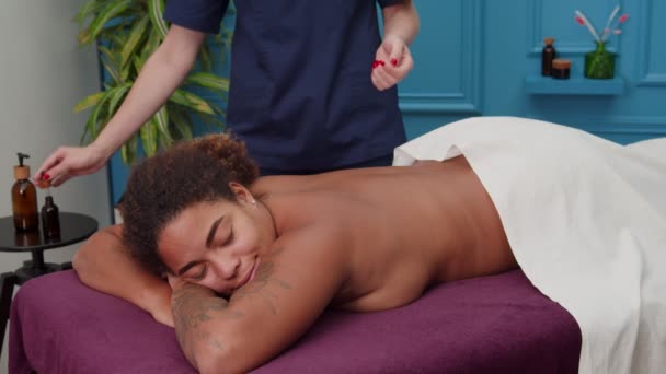 Massaggiatrice versando olio massaggiante sulle braccia, massaggiando la donna in casa — Video Stock