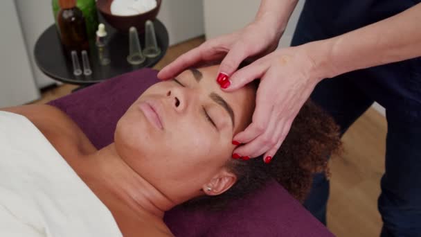 Masajista aplicando loción facial, masajeando la frente de las mujeres en interiores — Vídeos de Stock