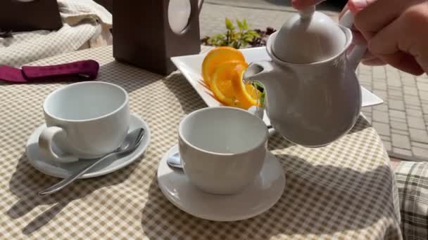 Unrecognizable human hand taking teapot, pouring tea into cup outdoors — Stock Video