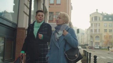 Dışarıdaki dükkanın camına bakan yaşlı kadınlar, merdivenlerden yukarı çıkan kadınlar.