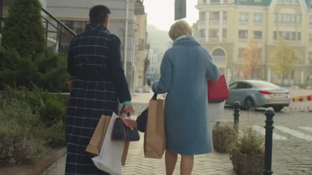 多くの店の紙のパッケージを運ぶ成熟した女性の背面図屋外 — ストック動画